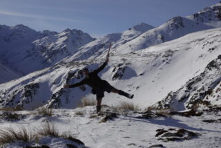 Man in mountains, doing star pose with ice axe.